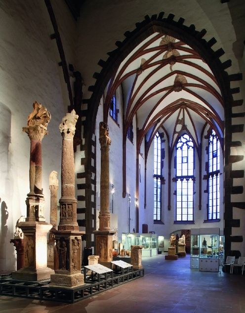 Blick in die Ausstellung im Seitenschiff der Klosterkirche mit Säulen im Vordergrund und Vitrinen im Hintergrund